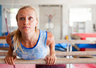 Woman gymnast performs complex acrobatic exercise on parallel bars in gym