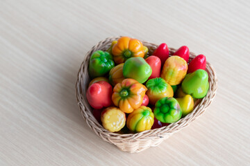 Colorful Thai mung bean desserts (look choop) shaped like mini fruits and vegetables, displayed beautifully in a wicker basket on a wooden table. Traditional Thai sweet.