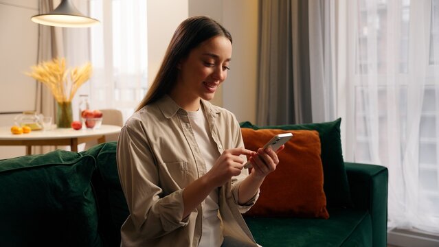 Caucasian woman girl female lady using mobile phone apps modern technology website at couch at home in living room relaxation browsing smartphone application social media order food delivery online - Powered by Adobe