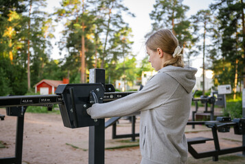 Young woman training on outdoor gym machine in park on a sunny day