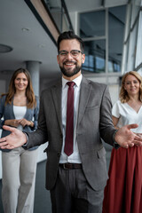 Fototapeta premium Smiling businessman welcoming people with open arms in office hallway