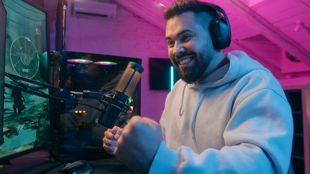 Excited winner champion Caucasian guy male gamer streamer man winning luck achievement victory internet win talking microphone play online game addict in headphones gaming streaming in neon dark room