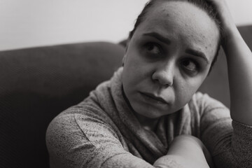 A woman sits on a couch in a dimly lit room her expression thoughtful and contemplative She rests...