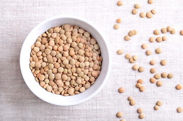 Plate lentils in a white bowl on linen fabric. Unshelled, dried and large green lentil variety, typically of flat shape, that hold their shape when cooked. Used in soups, stews, or salads. Food photo