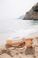 Stylish beach toys set. A close-up summer beach scene with a pastel-colored swim ring, a toy bucket, and sand molds lying on the sand shore. 