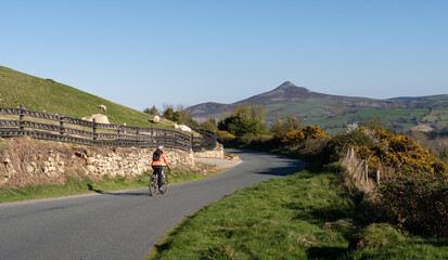 Fototapeta premium Weekend getaway. A female cyclist rides through the mountainous landscape of Wicklow, Ireland, with Sugar Loaf Mountain on the horizon.