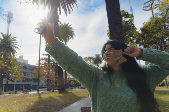 Young Venezuelan woman in the square taking a selfie with her phone and a dry leaf