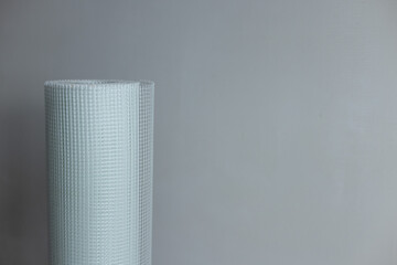 A roll of white plaster mesh for preparatory and painting works on a grey background .