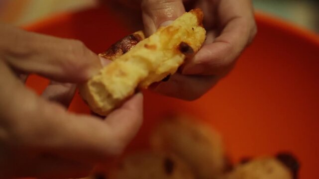 M&atilde;os repartindo um p&atilde;o de queijo quentinho.