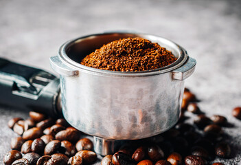 Close-up ground coffee in portafilter and roasted coffee beans or filter coffee handle on gray...