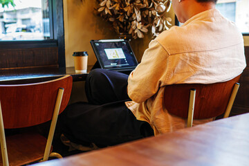 Rear view of relax man sitting looking at tablet with paper coffee cup on table at coffee shop