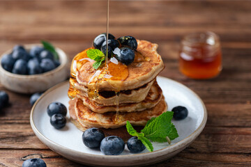 Healthy oat pancakes with blueberries and maple syrup, rustic wooden table background