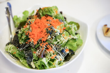 Green vegan salad from green leaves mix and vegetables, top view on white table. Green salad, close up by green vegetable, seaweed, and tobiko dressing on a white plate, isolated on white background.