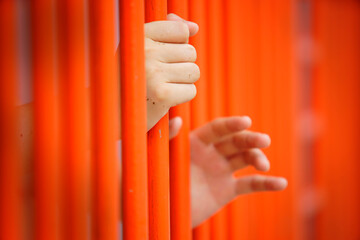 Obraz premium Close-Up View of Hands Grasping Bright Orange Prison Bars