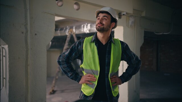 Happy proud Caucasian guy holding hands on hips in construction manufactory architect man technician posing glad electrician male feeling satisfied pleased cheerful inspector contractor admiring work