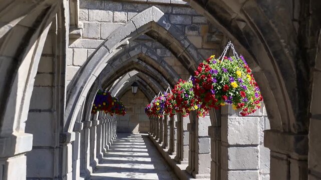 row of rustic stone archways adorned with colorful hanging flowers forms a charming path through an old world courtyard evoking peaceful garden walks and romantic historic settings for travel and