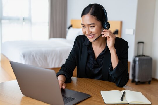 Professional woman working remotely with headset and laptop in a hotel room, managing communications online.