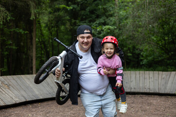 Happy father carrying smiling daughter while holding a balance bike after a successful training...