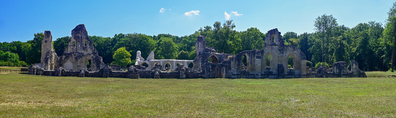 Panoramic photo of the remains of Vauclair Abbey in the French village of Bouconville-Vauclair. With forests in the background and a clear blue sky.