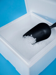 Close-up view of black plastic scoop filled with dry ice pellets inside white insulated container