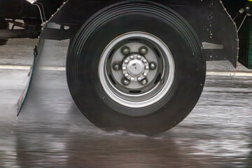 Detail of the wheel of a truck driving on a wet road during rain.