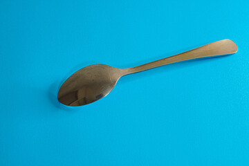 A stainless steel spoon lies on a vibrant blue surface.