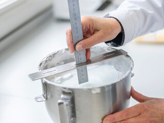 Laboratory technician measuring depth of liquid sample using precision ruler in steel container