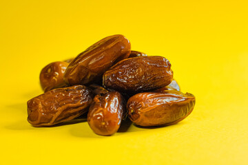 A close-up shot of a pile of fresh, brown dates on a yellow surface.