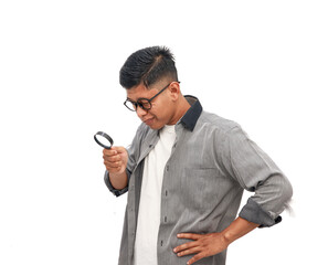 An Asian man wearing glasses intently examines something with a magnifying glass with curiosity and focus isolated on white background