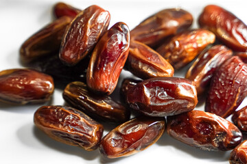 A close-up of a pile of shiny, brown dates on a white surface, showing their texture and color.