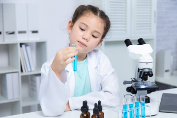 Young Caucasian student in lab coat girl analyzing test tube in science lab, concentrated face focused on experiment using glassware and microscope, elementary education learning, future scientist