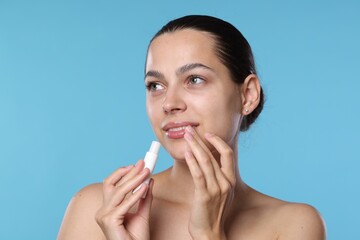 Young woman with lip balm on light blue background