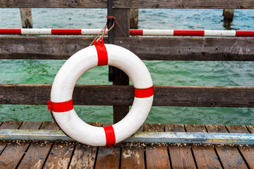 Lifebuoy hanging on wooden pier rail at lakeside for safety, rescue and nautical design concepts