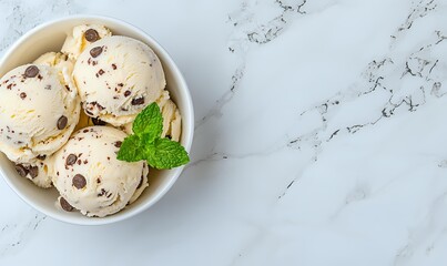 Creamy vanilla ice cream scoops with chocolate chips and fresh mint leaf garnish in white ceramic bowl on marble surface, top view with copy space.