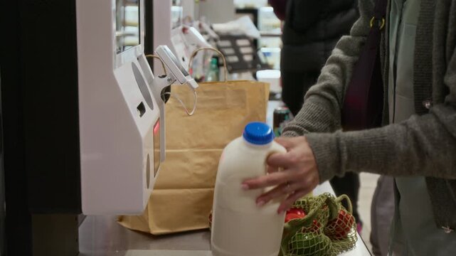 Midsection shot of anonymous female shopper scanning groceries at self-checkout and putting them in paper bag