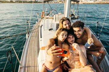Four friends are enjoying their time on a sailboat, drinking cocktails and taking a selfie