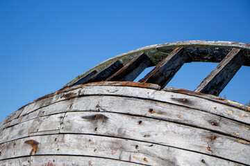 Weathered wooden boat hull reveals craftsmanship under clear blue sky near coastal location during...