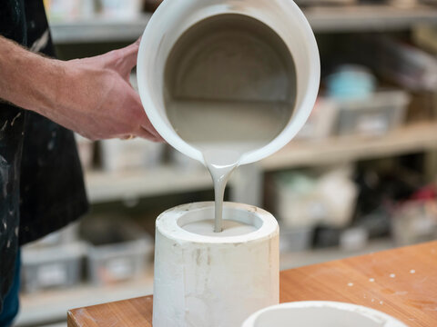 Potter pouring liquid slip into ceramic vessel demonstrating glazing process in traditional pottery workshop
