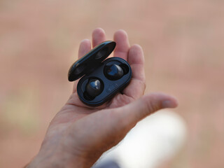 Open palm displaying black wireless earbuds in charging case showing compact portable audio...