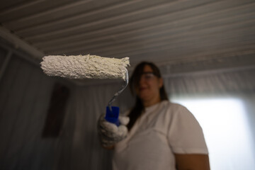 A woman in protective gear skillfully paints a ceiling with a roller, concentrating on home...