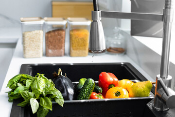 Fresh vegetables and fruits are washed in a special tray for vegetables. Drops of water are poured on the vegetables in the sink. Concept of healthy nutrition and organic food