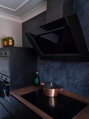 Modern kitchen featuring copper pot on induction cooktop, black range hood and blue textured...