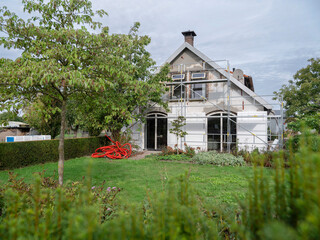 Residential property under renovation with construction scaffolding, landscaped garden, and home...