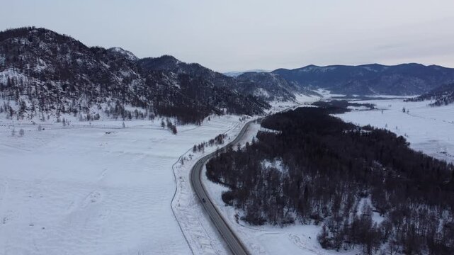 Aerial footage of a winding snow-covered road leading to Ust-Koksa in the Altai Republic, Russia. The video shows scenic winter landscapes with forests, hill