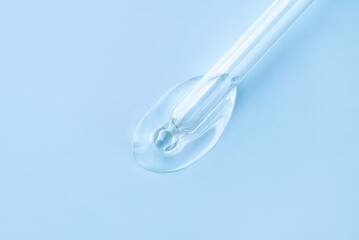 Drop of cosmetics and a pipette on a blue background. A product for skin, face or hair care.