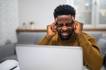 Overworked African American businessman having a headache while working remotely on laptop at his...