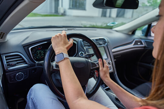 Woman holding steering wheel while driving modern car in city. Female driver controls vehicle, inside view. Safe driving and modern lifestyle concept