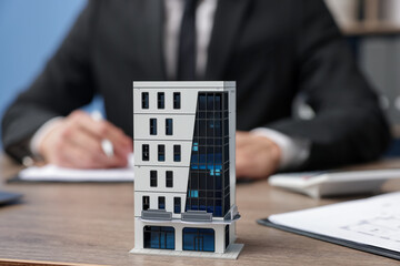 Real estate agent working at desk in office, focus on house model
