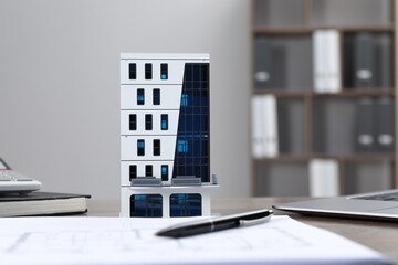 Real estate. Apartment building model, floor plan and laptop on table indoors, selective focus