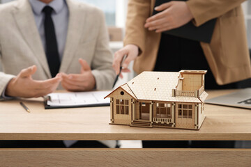 Real estate agent working with client at desk in office, focus on house model